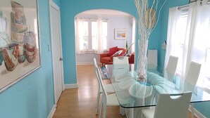 A dining area with a glass table and chairs, a red sofa, and a white cabinet.