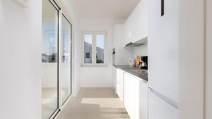 A modern kitchen with a sliding glass door leading to a balcony, a window, and a countertop with a coffee maker. - Awesome home in Punat (Punat)