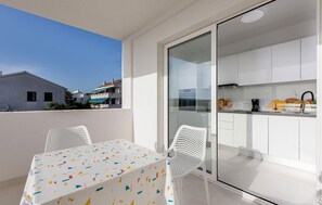 A balcony with a table and chairs, a sliding glass door leading to a kitchen, and a view of buildings in the background. - Awesome home in Punat (Punat)
