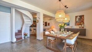 Un intérieur moderne avec un escalier en colimaçon, un coin repas avec une table en bois et des chaises blanches, et une cuisine agrémentée d’un grand tableau.