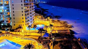 A high-rise hotel with multiple balconies, a pool area, and a beach view.