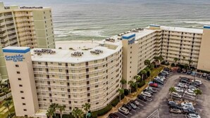 A beachfront hotel with multiple balconies, a parking lot, and a view of the ocean.