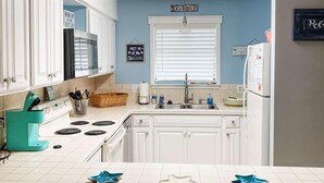 A kitchen with white cabinets, a stove, and a sink. There are signs on the wall, including one that says "Beach Life is the Best Life."