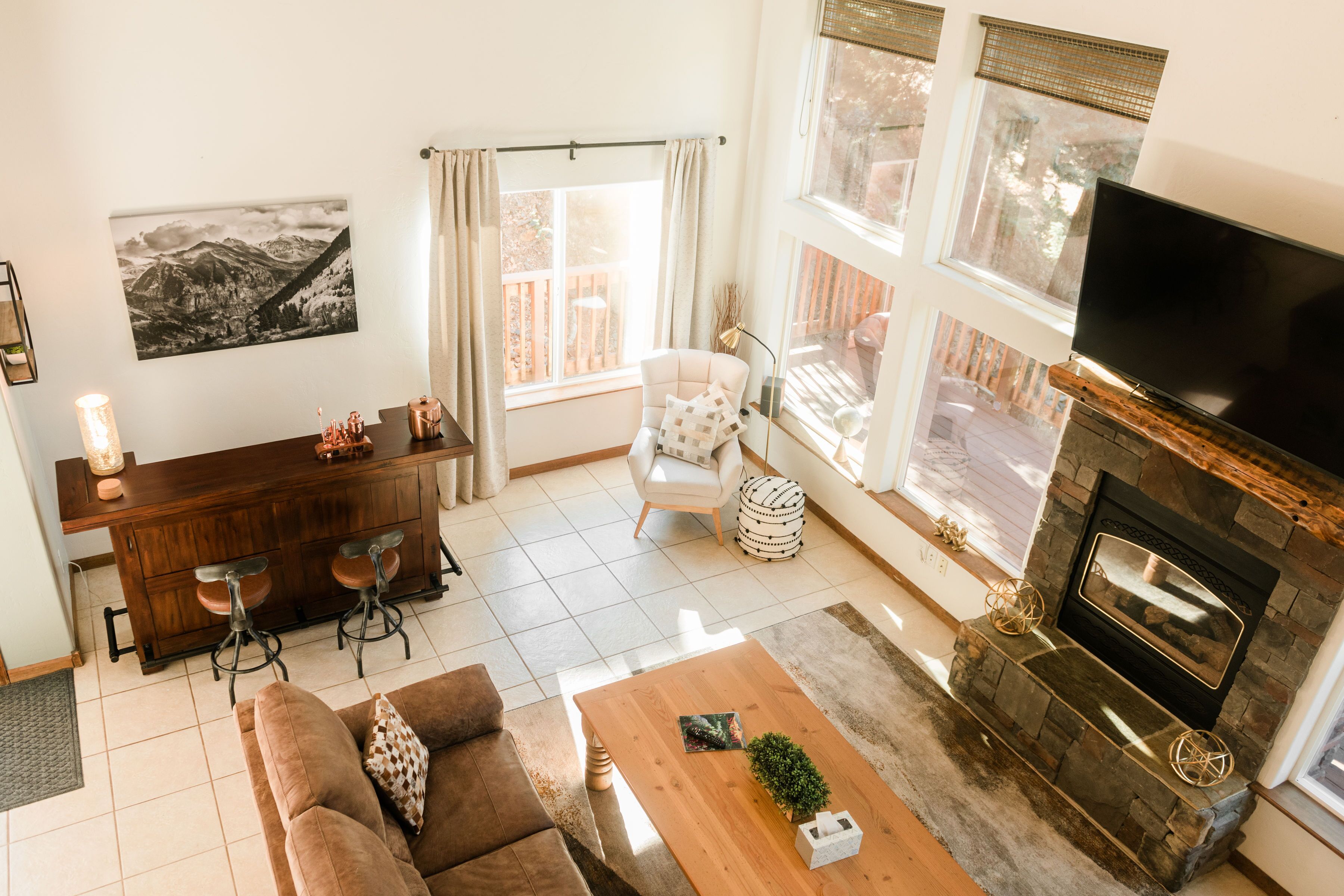 A modern living room with a fireplace, a TV, a dining area with bar stools, and a large window with curtains.