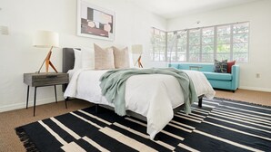 A bedroom with a bed, bedside tables, a blue sofa, a large window, and a black and white striped rug. - Courtyard at Lake Lucerne (Orlando)