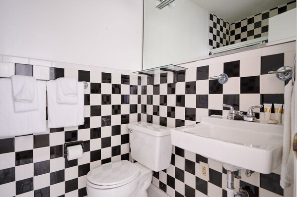 A bathroom with a black and white checkered tile backsplash, a white toilet, a white sink with a mirror above it, and two white towels hanging on the wall. - Courtyard at Lake Lucerne (Orlando)