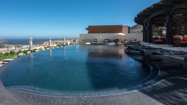 Ein Infinity-Pool mit Meerblick, Sitzgelegenheiten im Freien und ein überdachter Bereich mit Sonnenschirmen.