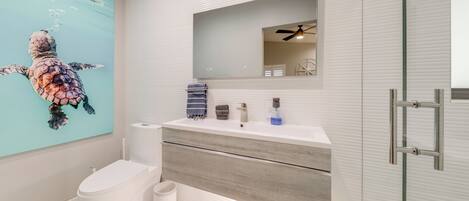 A modern bathroom with a white vanity, a large mirror, a ceiling fan, and a wall-mounted toilet.