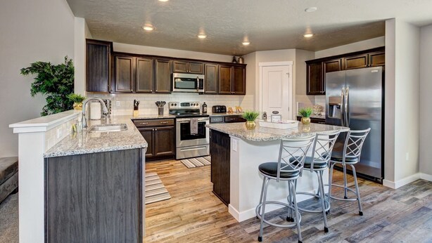 A modern kitchen with dark wood cabinets, stainless steel appliances, a granite countertop, and a bar area with stools. - South Nampa Family Home | Cali King | Game Loft | 5 TVs | Near Downtown Nampa (Nampa)