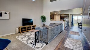 A modern living room with a grey sectional sofa, a flat-screen TV on a wooden stand, a small wooden table, and a patterned rug. - South Nampa Family Home | Cali King | Game Loft | 5 TVs | Near Downtown Nampa (Nampa)