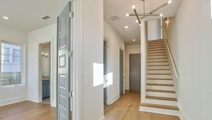 Un interior espacioso con una escalera de madera, una zona de cocina y un amplio ventanal que proporciona luz natural.
