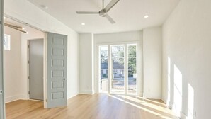 Amplia habitación con suelo de madera, ventilador de techo y grandes ventanales que dejan entrar luz natural.