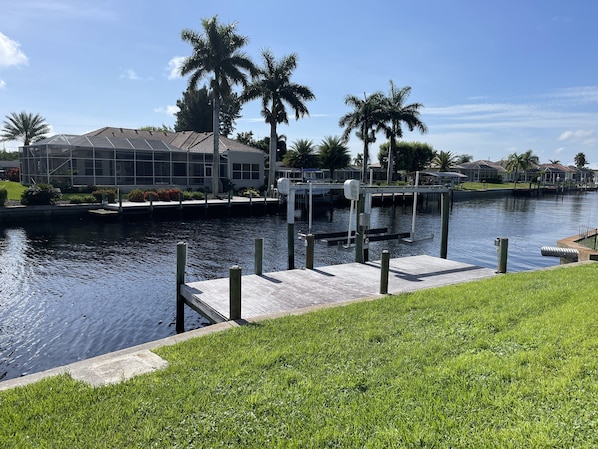 A waterfront property with a dock, palm trees, and a house with a tiled roof.
