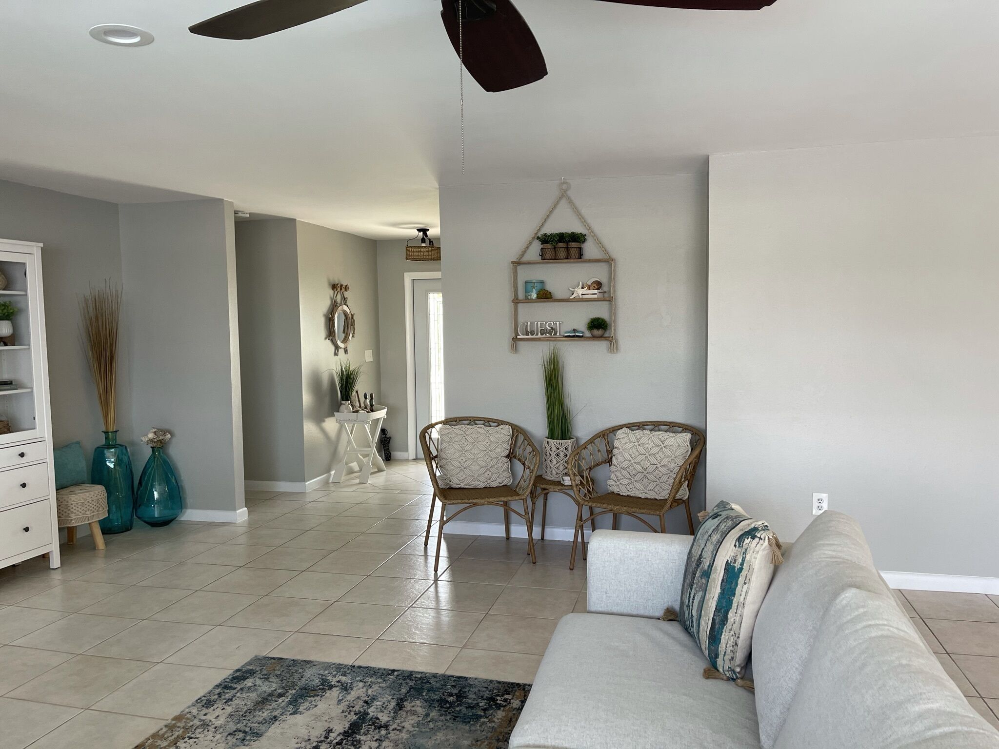A spacious living room with a white sofa, two wicker chairs, a coffee table, and a decorative wall shelf.