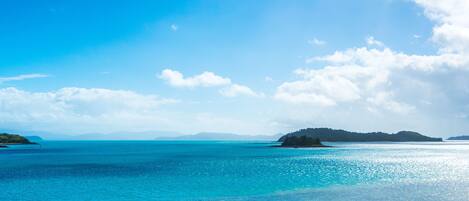 A coastal landscape with clear blue water, a distant island, and a clear sky.