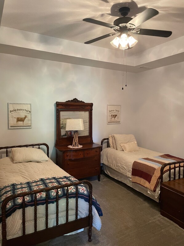 A bedroom with two beds, a ceiling fan, and a dresser.