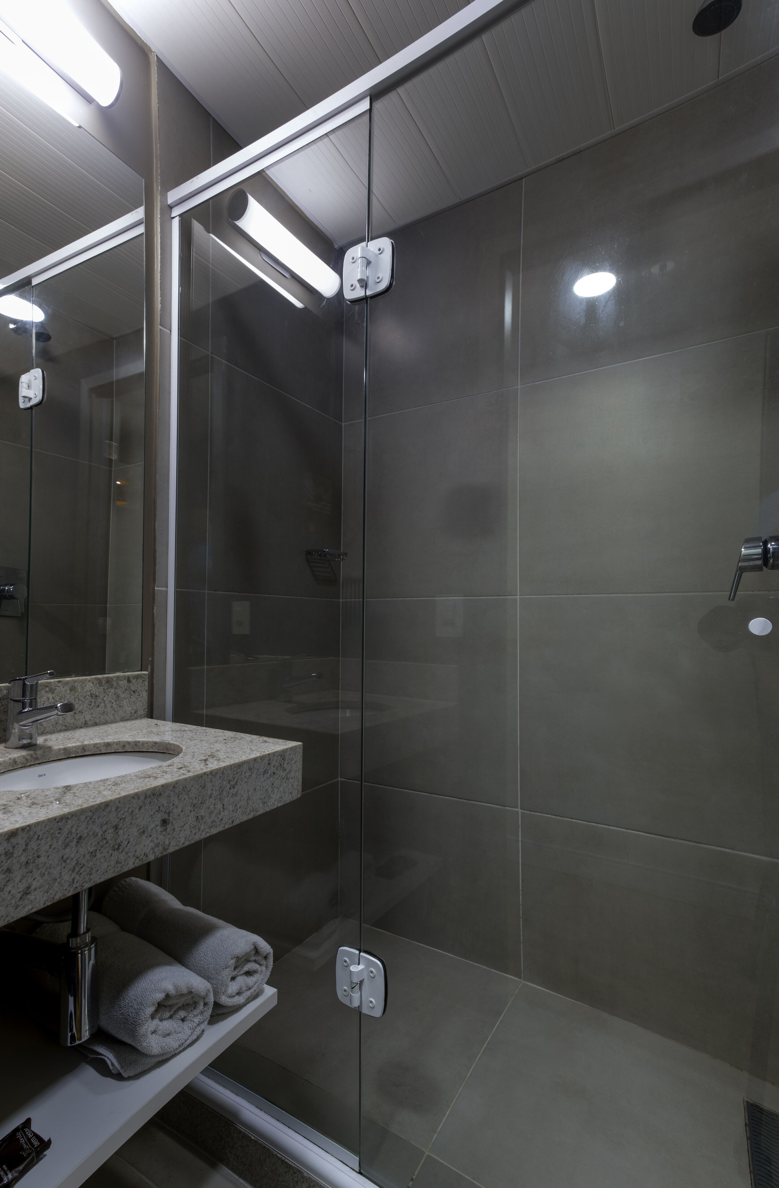 A modern bathroom with a glass shower enclosure, a granite countertop sink, and a towel rack.