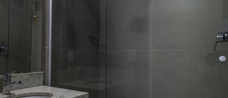 A modern bathroom with a glass shower enclosure, a granite countertop sink, and a towel rack.