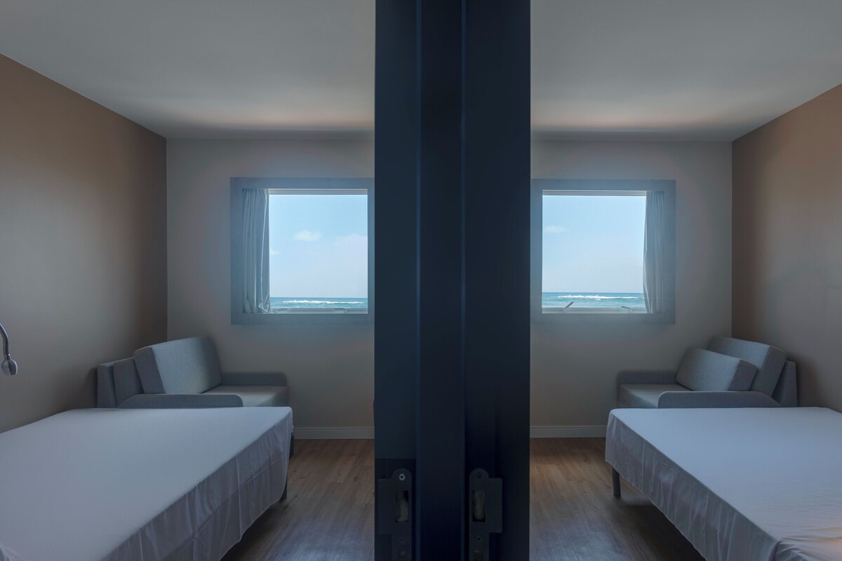 Une chambre avec deux lits, une grande fenêtre et vue sur l’océan.
