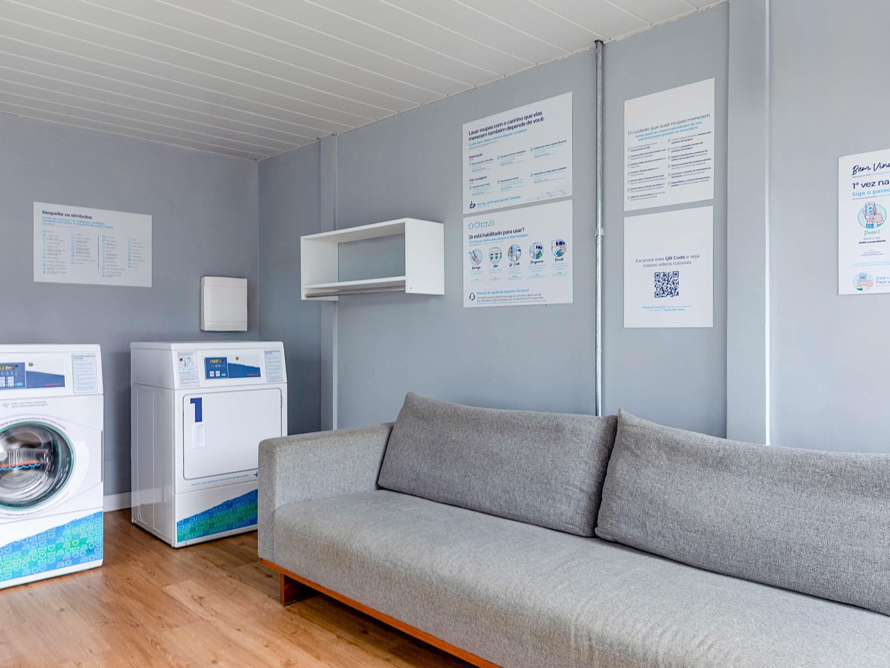 Ein moderner Waschraum mit zwei Waschmaschinen, einem grauen Sofa und informativen Postern an der Wand.