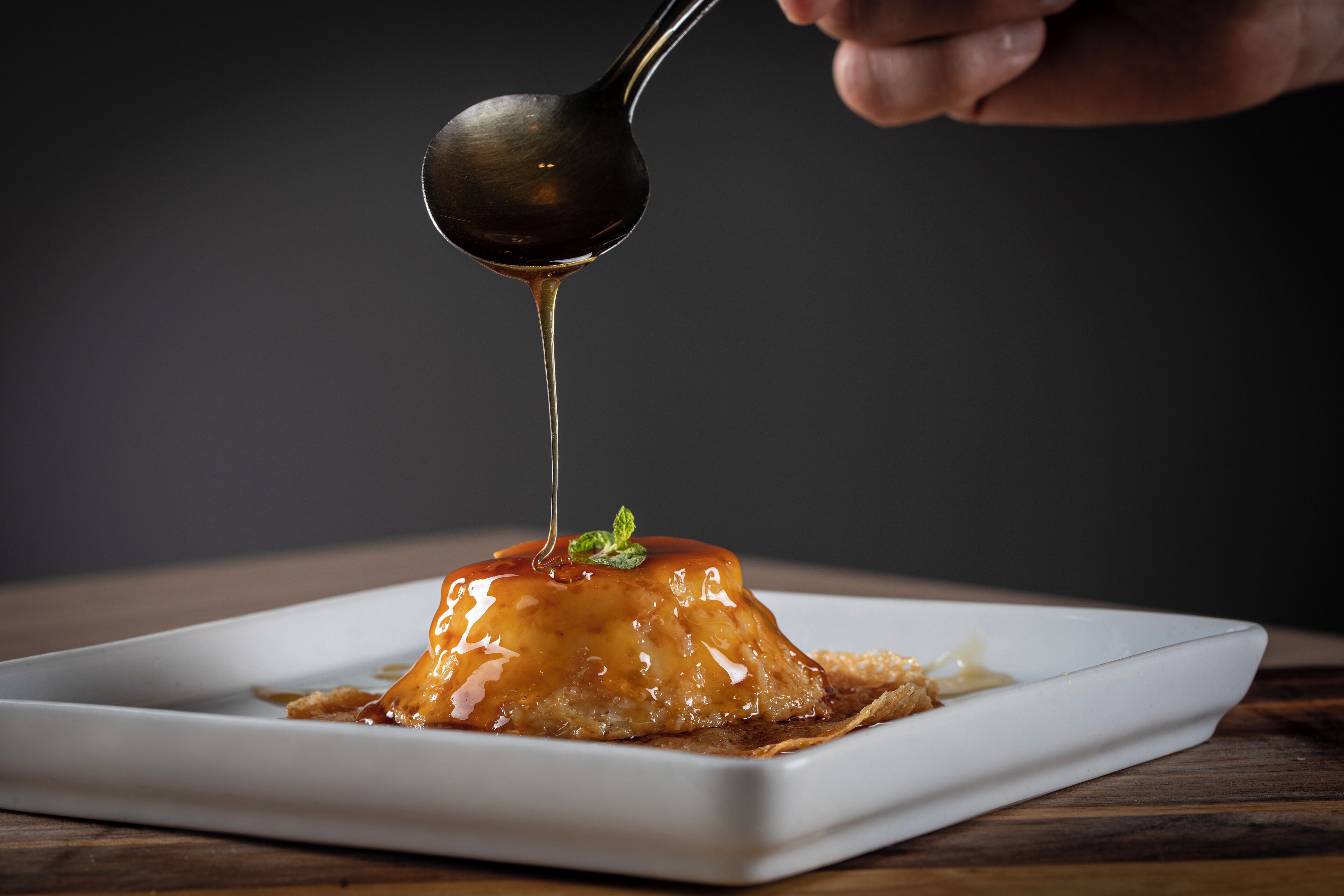 Un dessert servi dans une assiette blanche, avec une cuillère qui soulève une sauce au caramel.