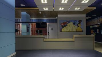 A reception area with a modern design, featuring a reception desk, a flat-screen TV, and a large abstract painting on the wall.