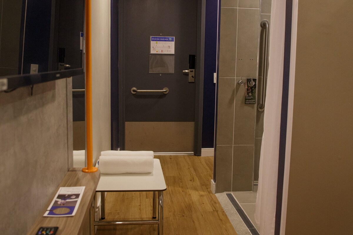 Une salle de bain d’hôtel avec un sol en bois, un porte-serviettes, un miroir et un espace douche.