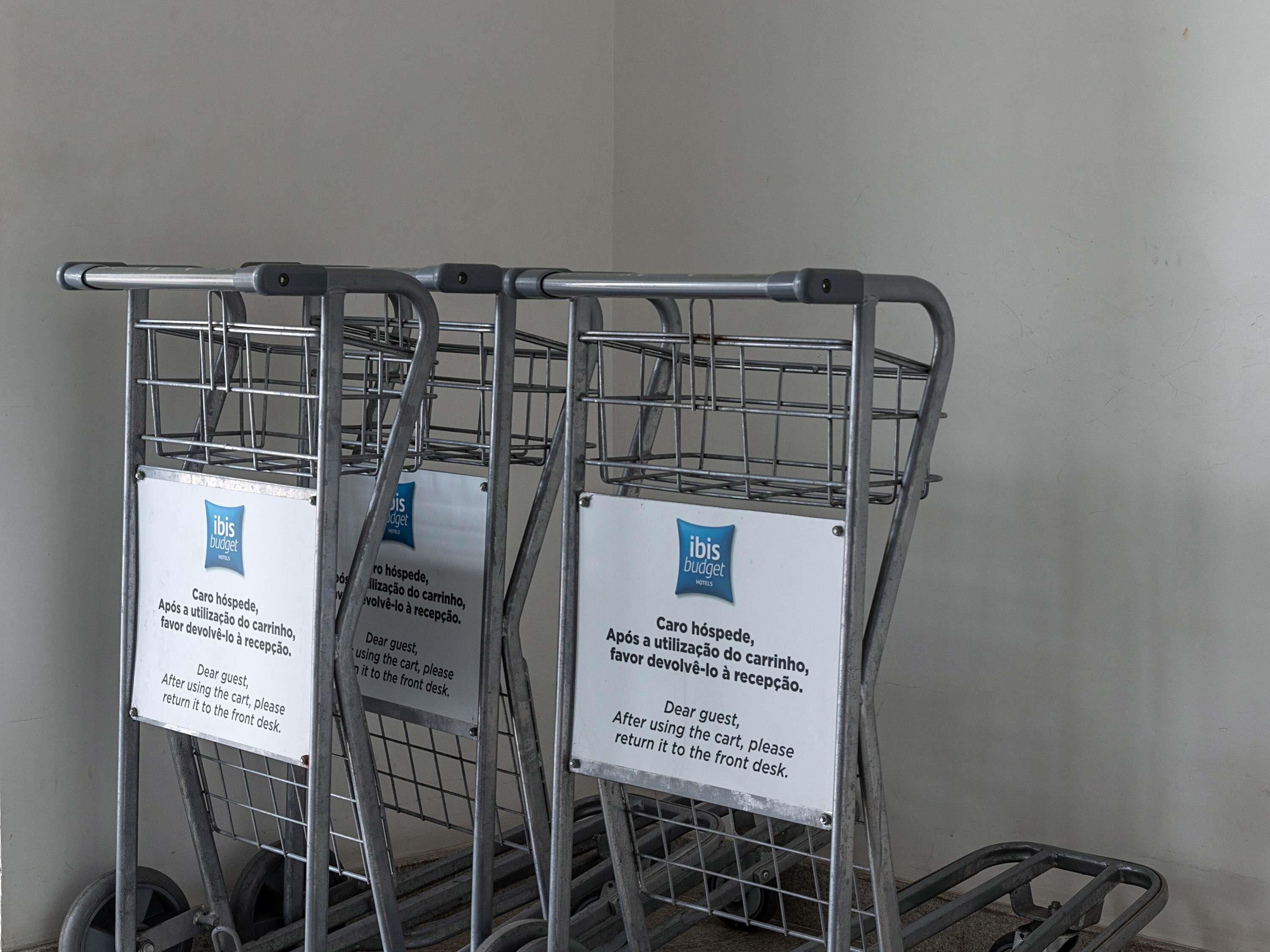 Three metal shopping carts with signs attached, indicating a request for guests to return the carts to the front desk after use.