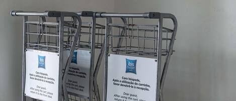 Three metal shopping carts with signs attached, indicating a request for guests to return the carts to the front desk after use.