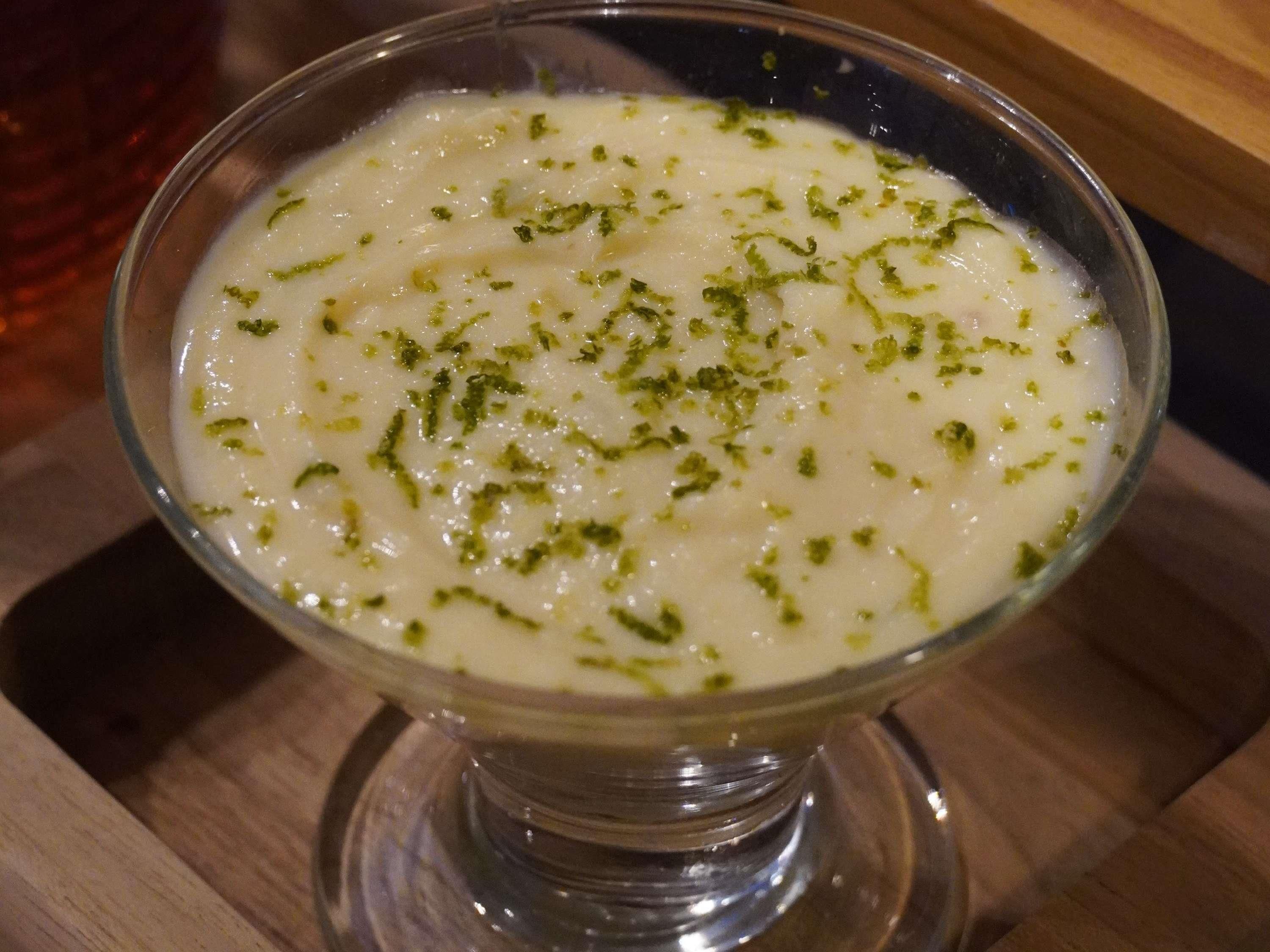 A clear glass bowl of a creamy white dessert garnished with green herbs, placed on a wooden surface.