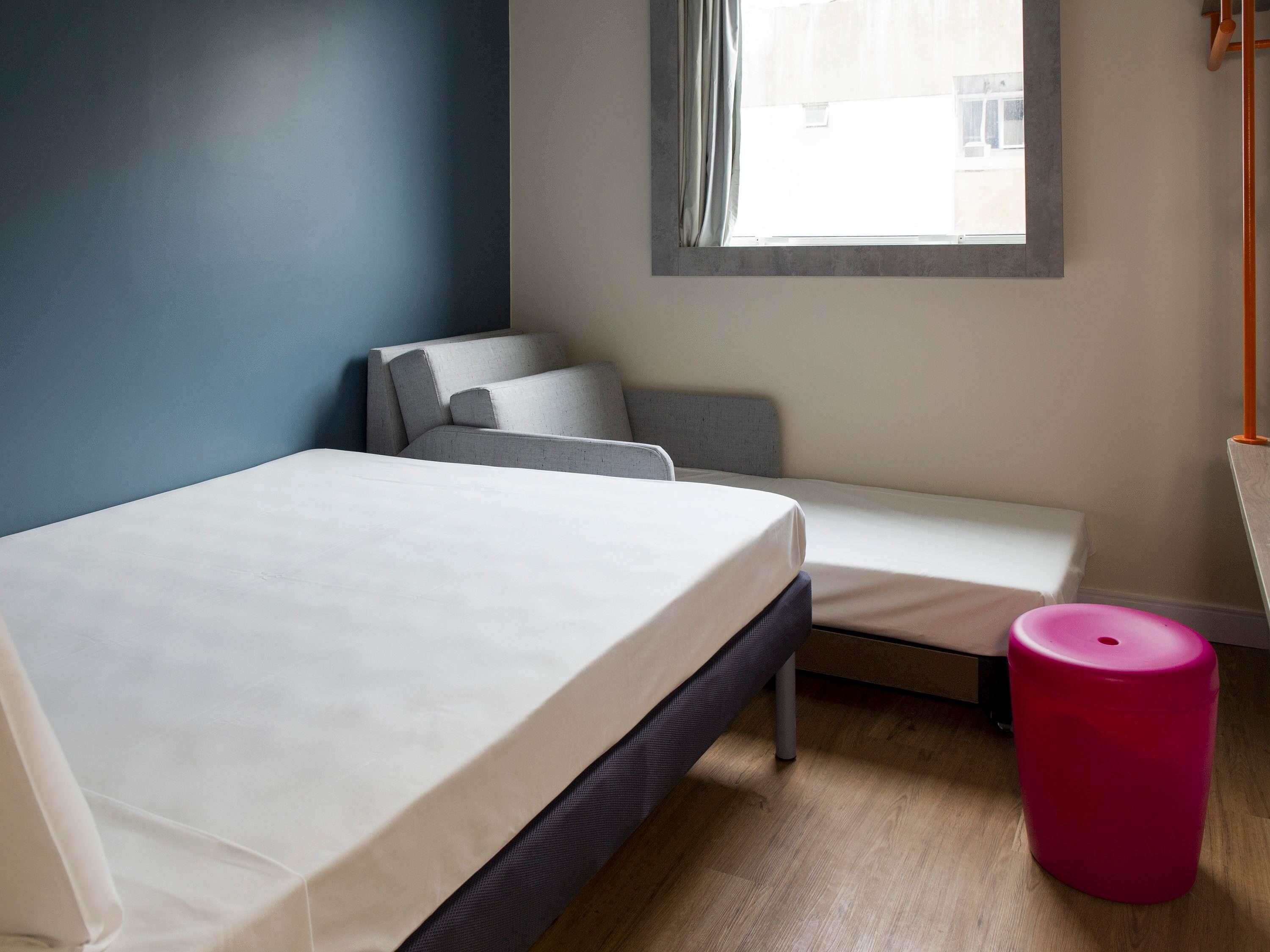 Een slaapkamer met een bed, een bankje en een roze kruk.