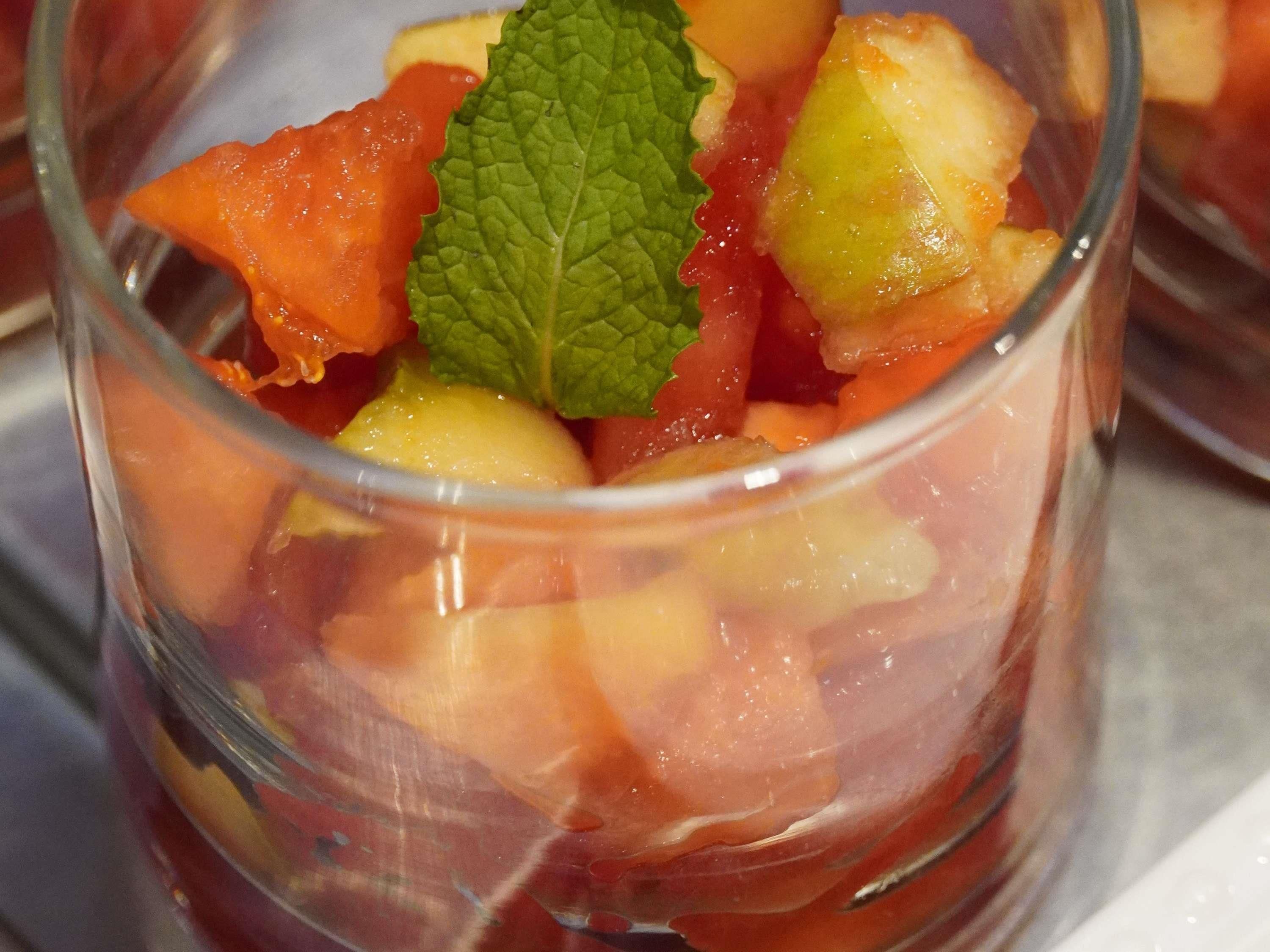 A glass containing a fruit salad with a mint leaf garnish.
