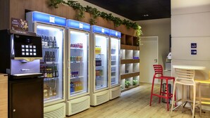 Uma área de bar com uma máquina de café, três dispensadores de bebidas e um conjunto de assentos com duas cadeiras e uma mesa.