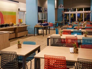 A restaurant with multiple tables and chairs, a counter with a display, and a view of the street through large windows. - ibis budget Maceió Pajuçara (Maceió)