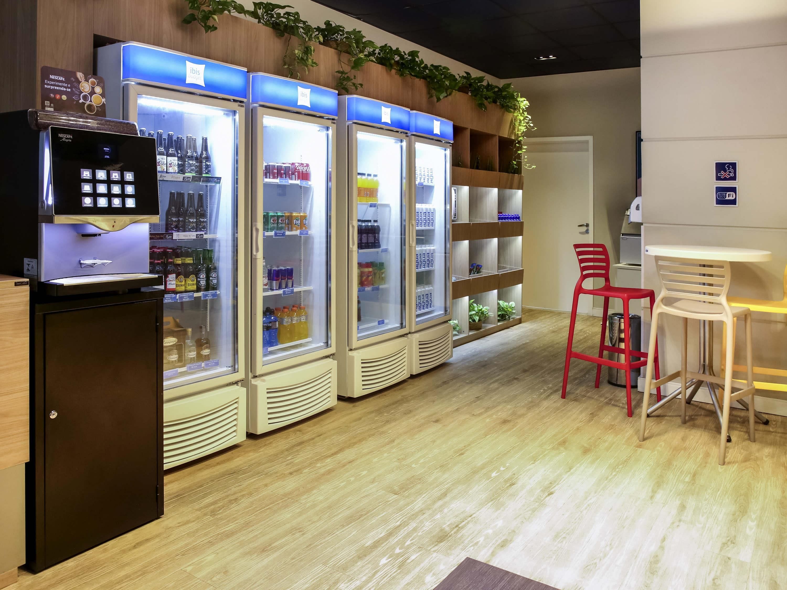 Uma área de bar com uma máquina de café, três dispensadores de bebidas e um conjunto de assentos com duas cadeiras e uma mesa.