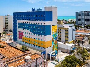 A multi-story hotel with a blue and yellow facade, a large mural, and a view of the ocean. - ibis budget Maceió Pajuçara (Maceió)
