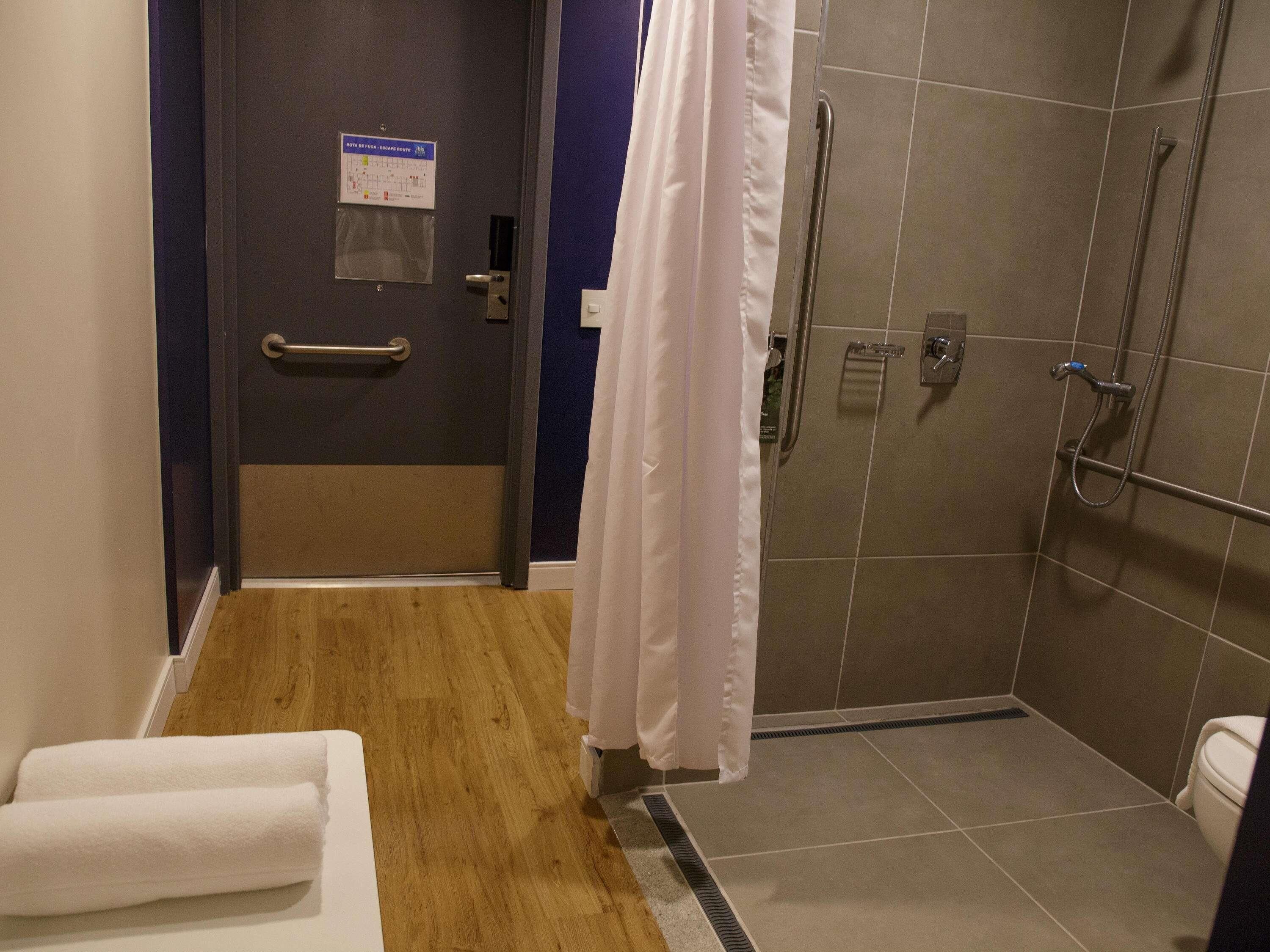 A bathroom with a shower, a toilet, a towel rack, and a door with a handrail.