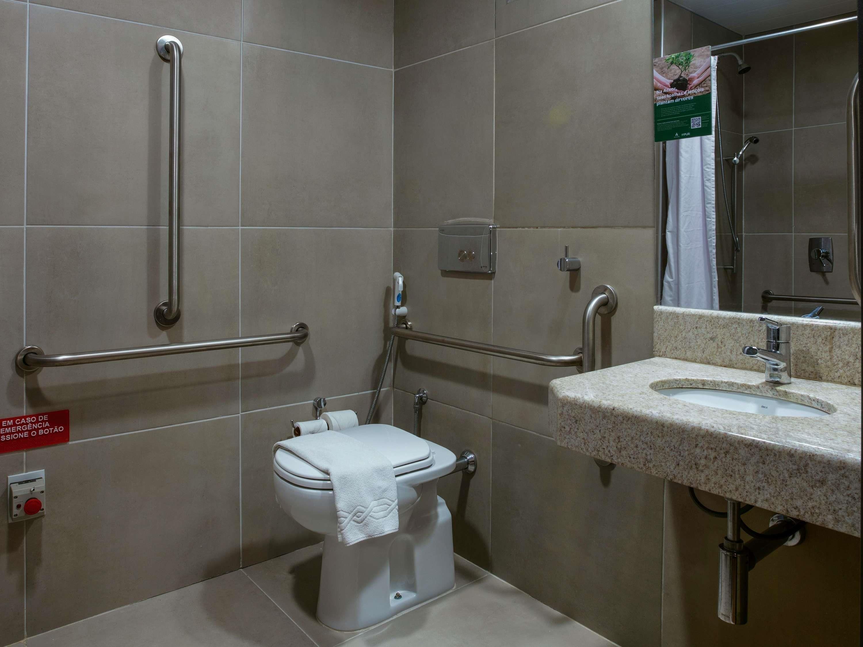 A bathroom with a toilet, sink, and handrails.
