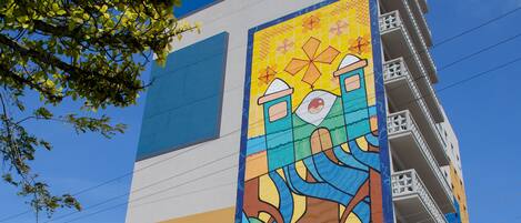 Un edificio con un mural colorido en la pared, una entrada azul y blanca, y un balcón visible.
