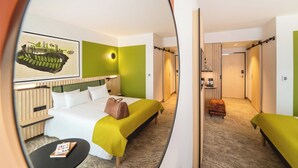 Una habitación de hotel con cama, mesita de noche y un pequeño rincón de descanso.