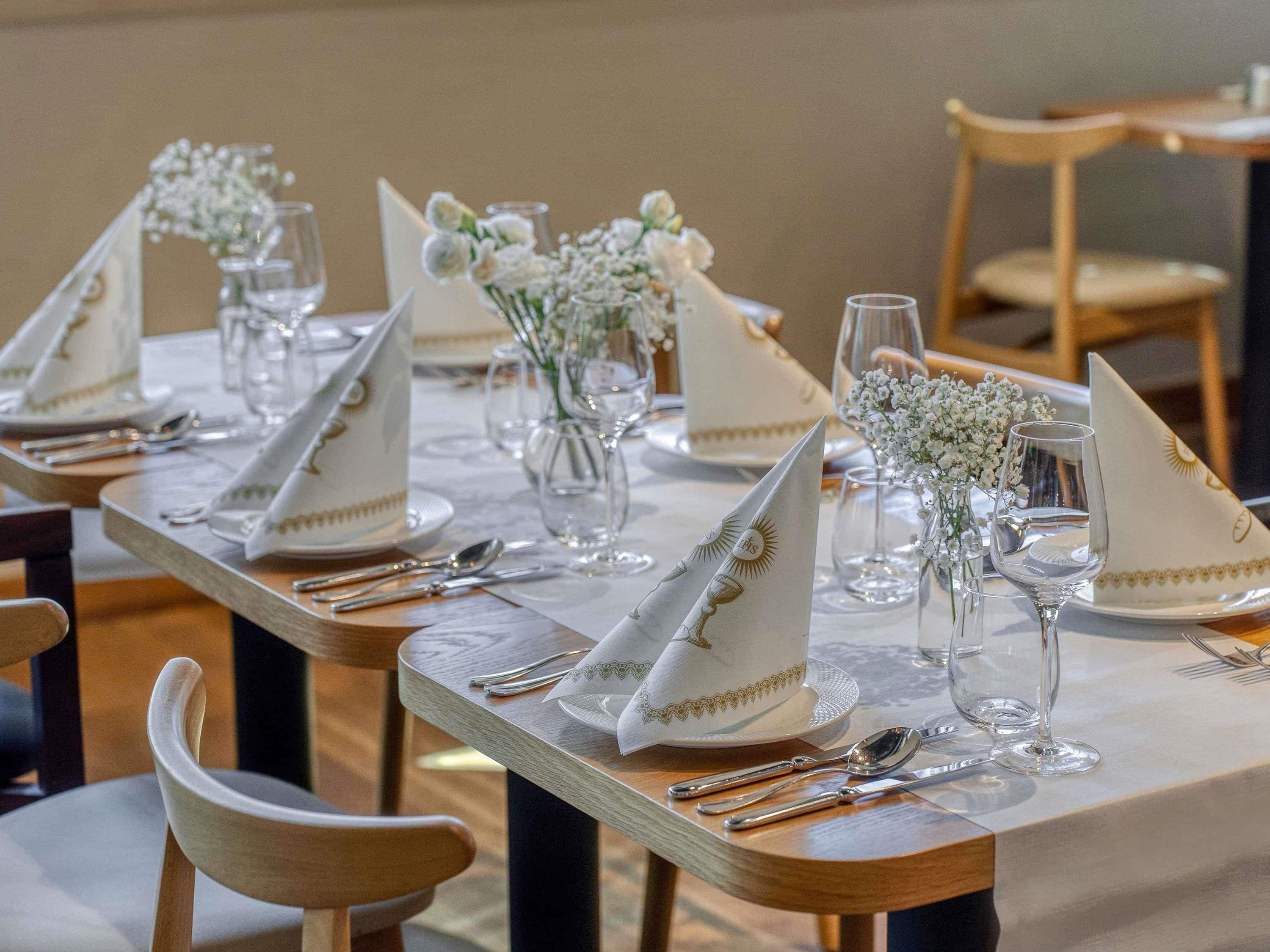 A dining table set with white napkins, silverware, and glassware, with small white flowers in vases.