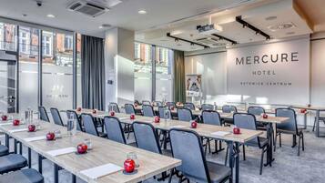 A conference room with multiple tables, chairs, and a large screen displaying 'Mercure Hotel Katowice Centrum'.