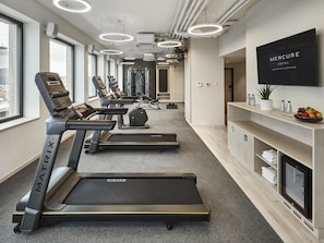 Un gimnasio moderno con cintas de correr, bicicletas estáticas y una televisión montada en la pared.