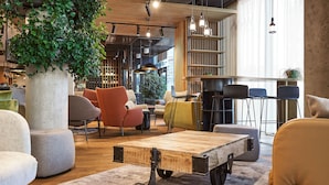 Un espacio lounge moderno con una mesa de centro de madera, asientos acolchados y una gran planta en maceta.
