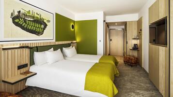 Quarto de hotel com uma cama grande, televisão, um pequeno espaço de estar e uma porta que dá para um corredor.