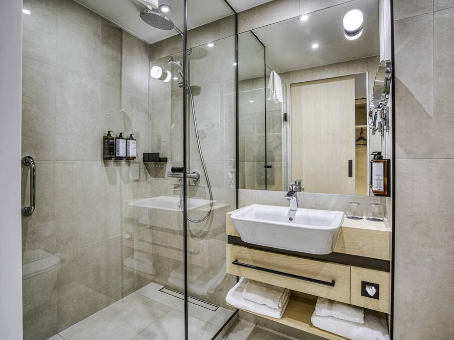 Un bany modern amb dutxa de vidre, un lavabo blanc i un mirall amb una pèrgola de fusta.