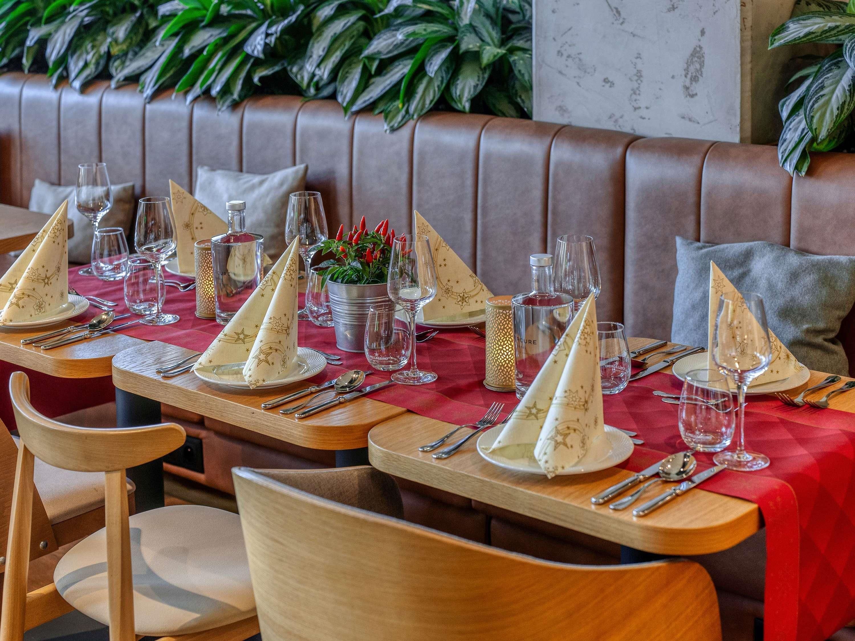 Un ambiente de restaurante con mesas dispuestas para comer, que incluye mantel rojo, servilletas blancas y cubiertos.