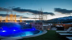Una piscina con cascada, rodeada de muros de piedra y una terraza de madera con sillones de descanso.