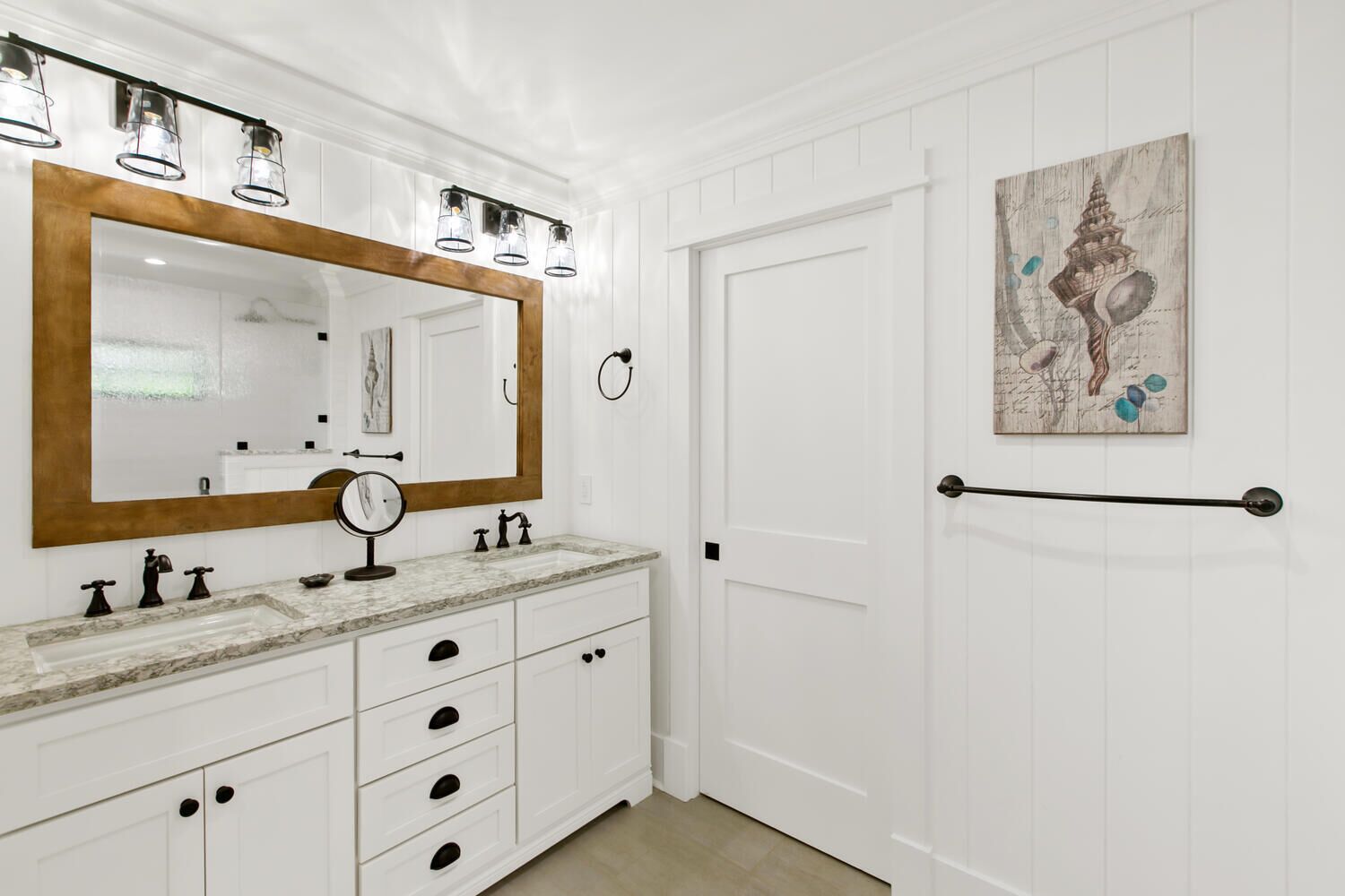 A bathroom with a large mirror, a vanity with a marble countertop, and a door with a towel rack.