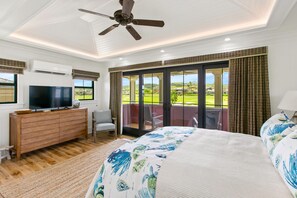 A bedroom with a large bed, a TV on a wooden dresser, a ceiling fan, and a balcony with a view of the outdoors. - Hale Moa'e by Alekona Kauai: Luxury 5br home with AC, private pool & spa, walk to Shops at Kukuiula (Koloa)